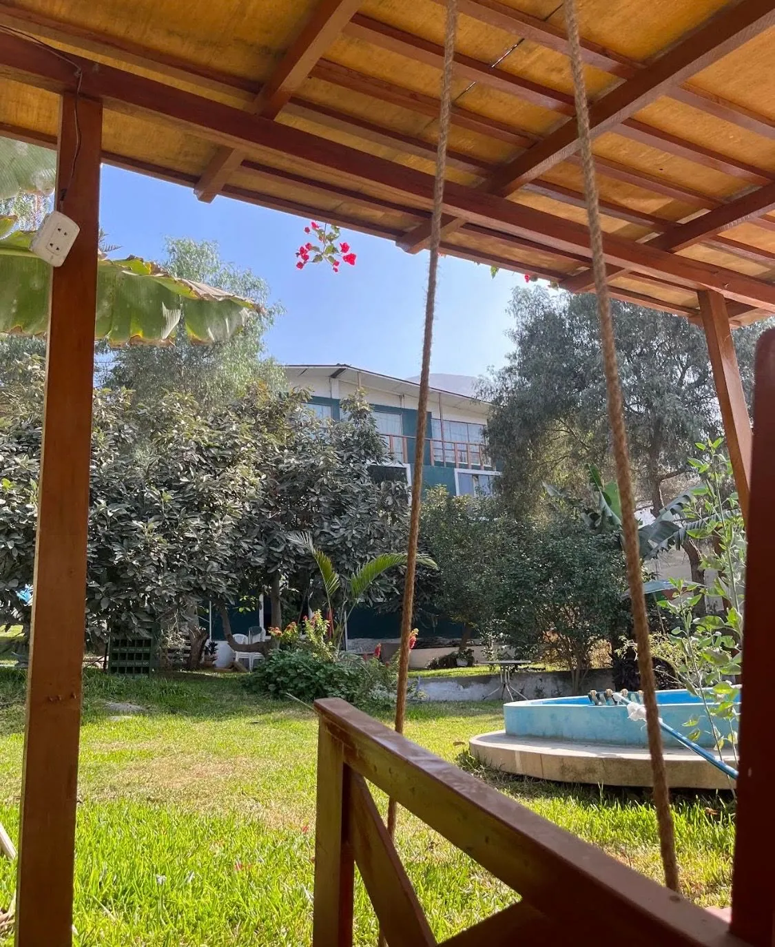 El jardín visto desde la pérgola de madera, con columpio, árboles y una fuente